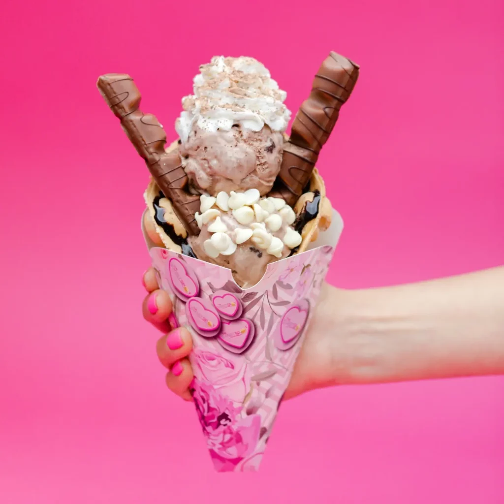 a hand Holding a bubble waffle cone, with two scoops of chocolate ice cream, whipped cream, and chocolate chips