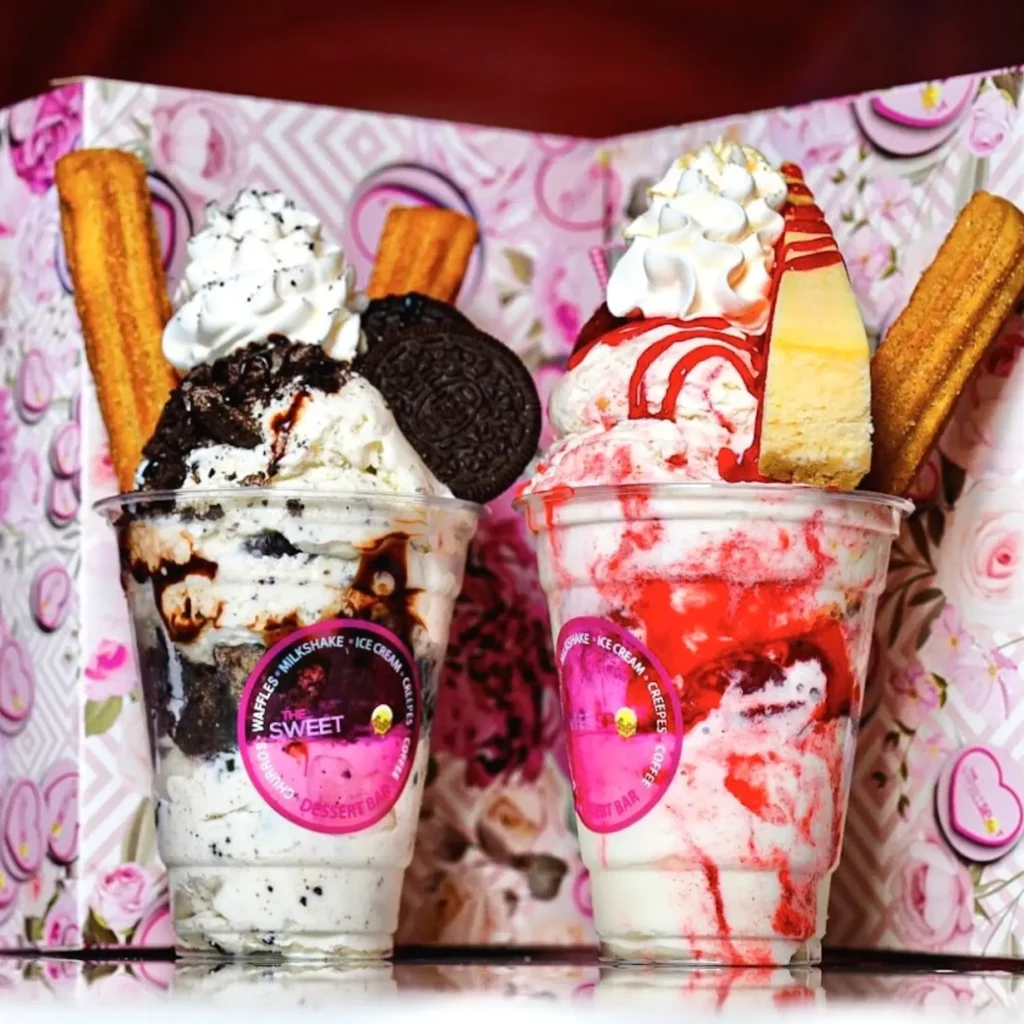 Two cups of ice cream. Oreo cookies and cream ice cream, strawberry cheesecake ice cream, whipped cream churros, and a piece of cheesecake.